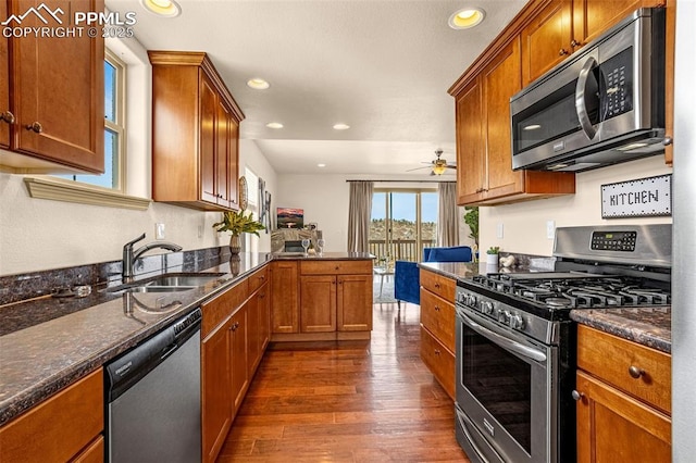 kitchen with dark wood-type flooring, sink, dark stone counters, kitchen peninsula, and stainless steel appliances