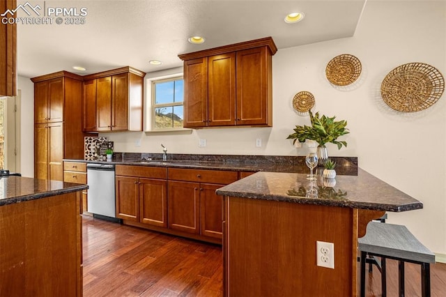 kitchen with dark wood-type flooring, sink, a breakfast bar area, stainless steel dishwasher, and dark stone counters