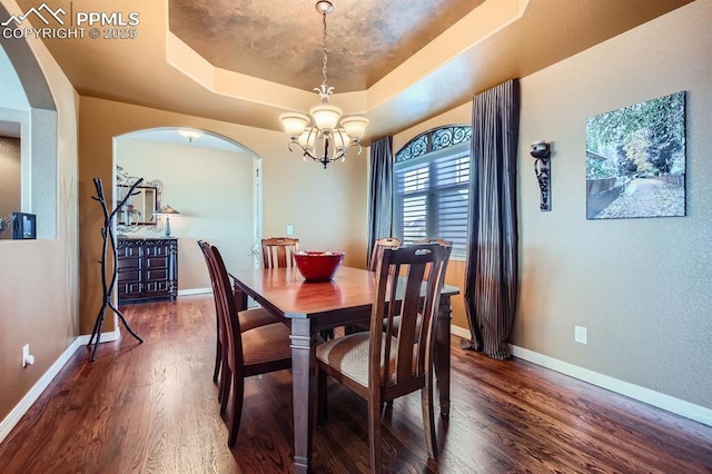 dining area with a raised ceiling, an inviting chandelier, and dark hardwood / wood-style flooring