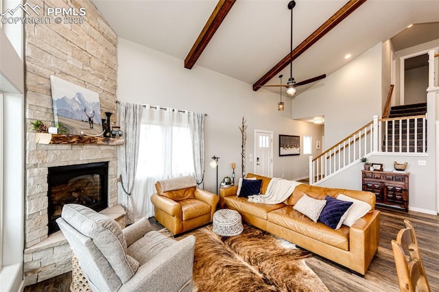 living room with hardwood / wood-style flooring, ceiling fan, high vaulted ceiling, a stone fireplace, and beamed ceiling