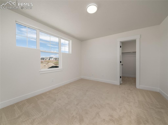 unfurnished bedroom featuring a closet, a spacious closet, baseboards, and light carpet