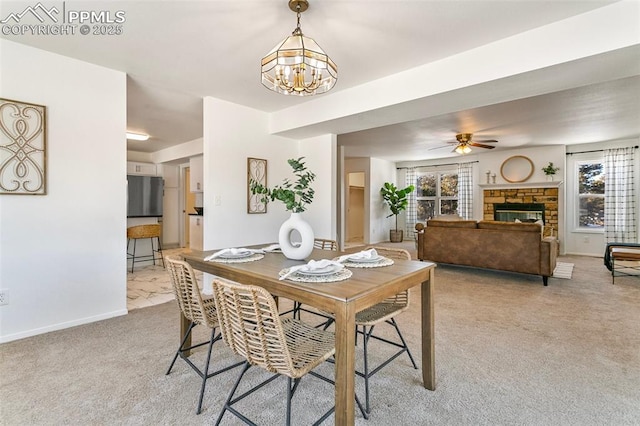 carpeted dining area with a stone fireplace and ceiling fan with notable chandelier