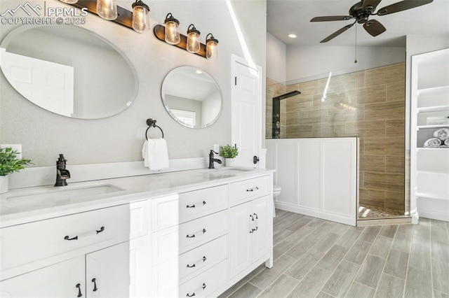 bathroom featuring hardwood / wood-style floors, a tile shower, vanity, ceiling fan, and toilet