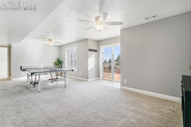 recreation room with a textured ceiling, light colored carpet, and ceiling fan