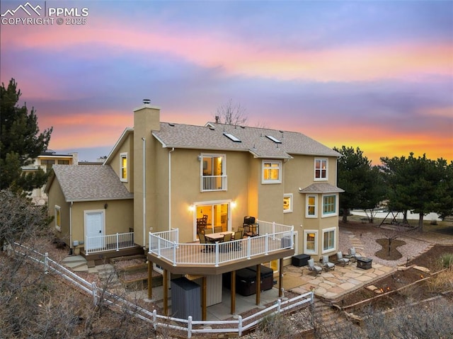 back house at dusk featuring a wooden deck and a patio