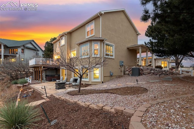 back house at dusk featuring an outdoor fire pit, a hot tub, a patio, and central air condition unit