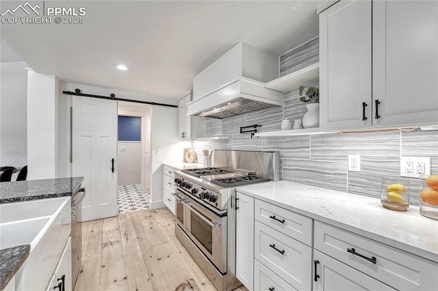 1636 Lakemoor Dr, Florissant, CO 80816 - kitchen featuring white cabinetry, double oven range, a barn door, light wood-style floors, and custom exhaust hood