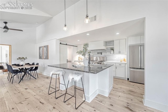 1636 Lakemoor Dr, Florissant, CO 80816 - kitchen with a barn door, white cabinetry, light wood-type flooring, stainless steel refrigerator, and a kitchen breakfast bar