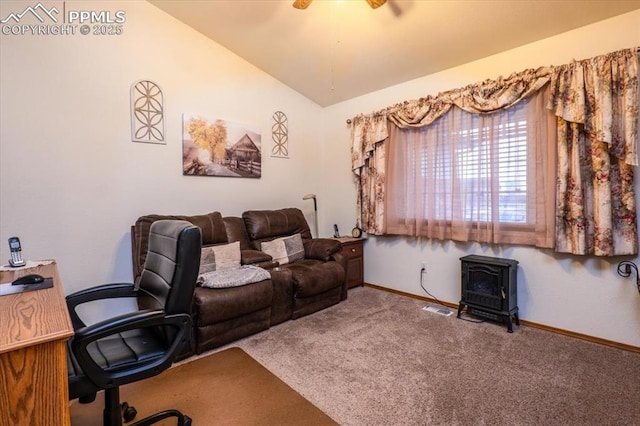 carpeted home office featuring vaulted ceiling, a wood stove, and ceiling fan