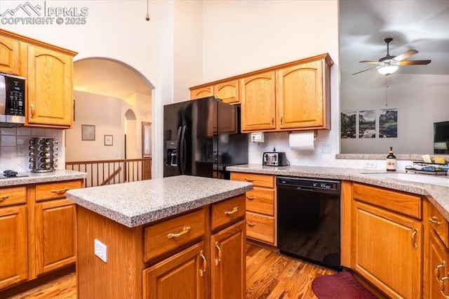 kitchen with a towering ceiling, light wood-type flooring, a kitchen island, and black appliances