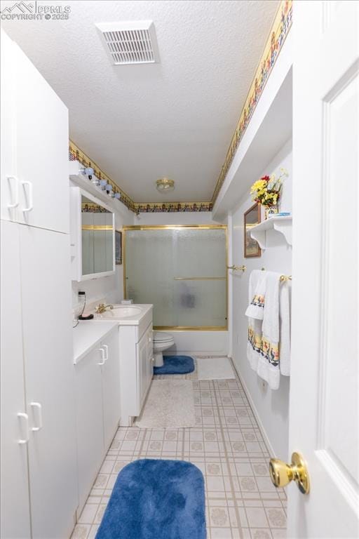 full bathroom featuring vanity, a textured ceiling, shower / bath combination with glass door, and toilet