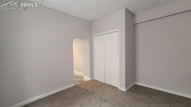 unfurnished bedroom featuring a drop ceiling, dark carpet, and a closet