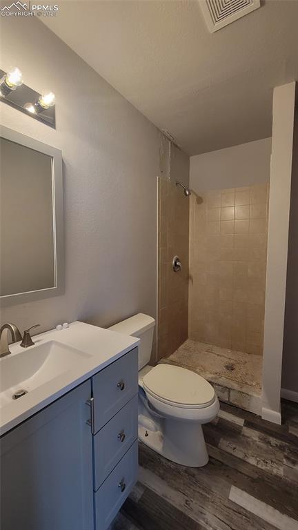 bathroom with vanity, wood-type flooring, toilet, and tiled shower