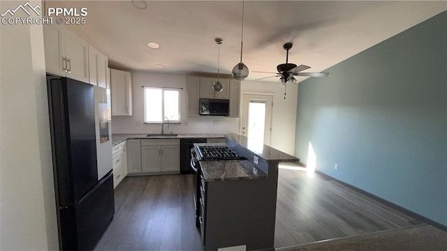 kitchen with dark stone counters, dishwashing machine, dark wood-type flooring, freestanding refrigerator, and a sink