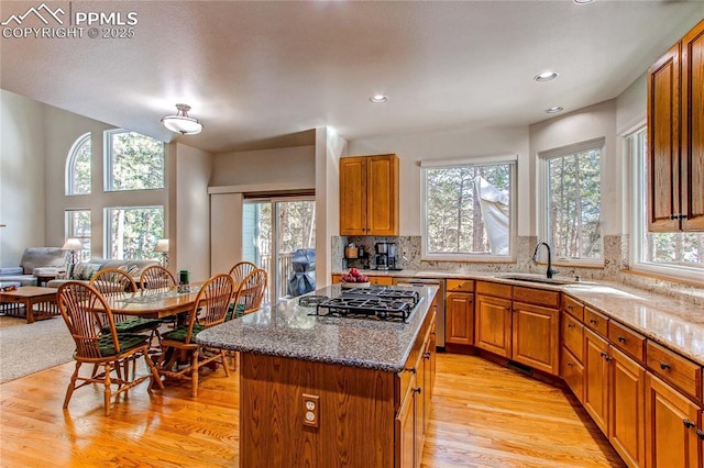 kitchen with sink, stainless steel gas cooktop, a center island, light stone countertops, and backsplash