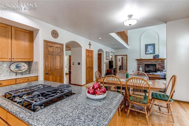 kitchen featuring stone counters, black gas cooktop, tasteful backsplash, a brick fireplace, and light wood-type flooring