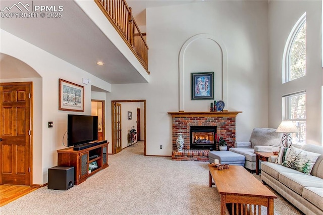 living room with a towering ceiling, carpet flooring, and a brick fireplace