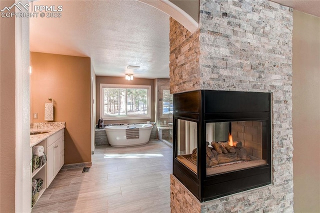 bathroom featuring vanity, a bath, a multi sided fireplace, and a textured ceiling