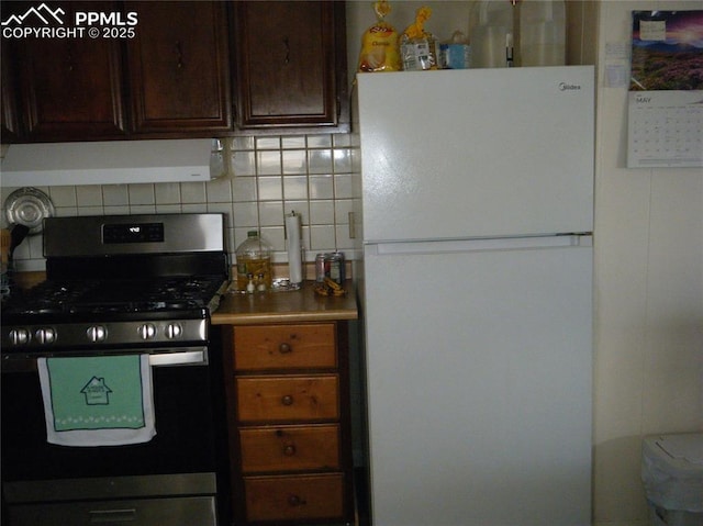 kitchen featuring dark brown cabinetry, decorative backsplash, range hood, freestanding refrigerator, and stainless steel gas stove