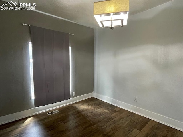 empty room featuring dark wood-type flooring, visible vents, and baseboards