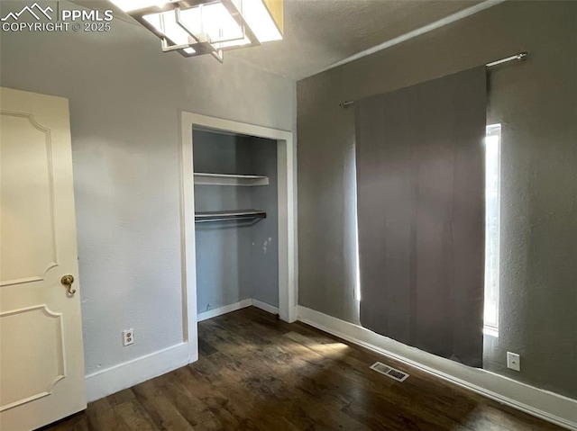 unfurnished bedroom featuring visible vents, baseboards, dark wood-type flooring, and a closet