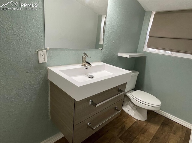 half bathroom featuring baseboards, toilet, wood finished floors, a textured wall, and vanity