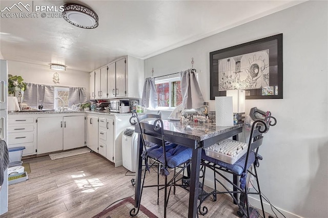 kitchen featuring light wood-style flooring, white cabinetry, light countertops, and a sink