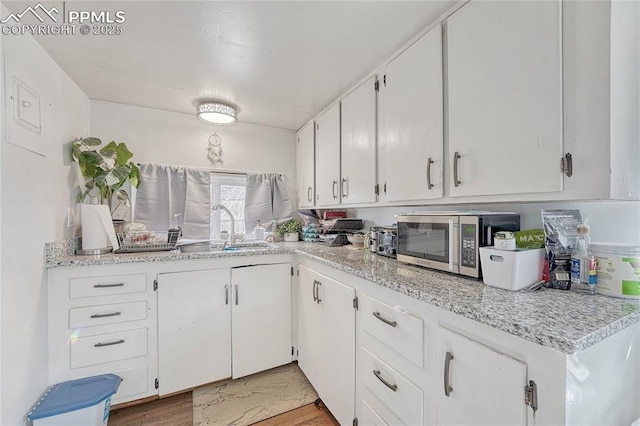 kitchen with a sink, stainless steel microwave, white cabinets, and light countertops