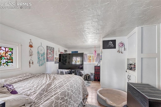 bedroom with heating unit, wood finished floors, and a textured ceiling