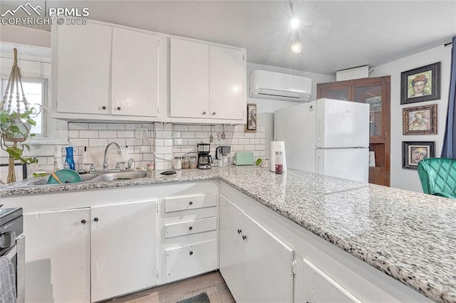 kitchen with freestanding refrigerator, a sink, an AC wall unit, white cabinets, and tasteful backsplash