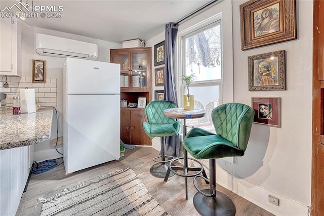 kitchen featuring tasteful backsplash, a wall mounted air conditioner, freestanding refrigerator, light wood-style floors, and white cabinetry