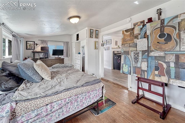 bedroom with baseboards, lofted ceiling, a textured ceiling, and wood finished floors