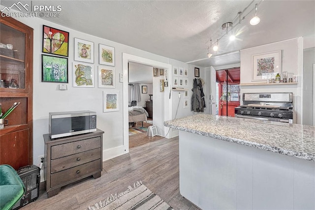 kitchen with wood finished floors, light stone countertops, stainless steel appliances, track lighting, and a textured ceiling