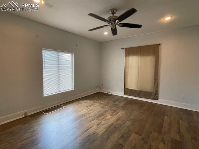 spare room featuring dark wood finished floors, visible vents, a ceiling fan, and baseboards