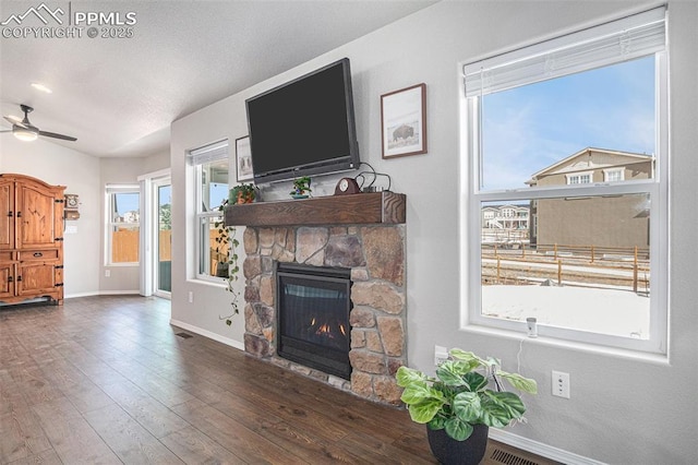 living room with dark hardwood / wood-style flooring, a stone fireplace, and ceiling fan