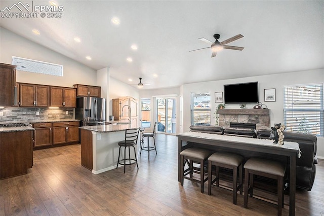 kitchen featuring an island with sink, sink, a kitchen breakfast bar, stainless steel fridge with ice dispenser, and light stone countertops