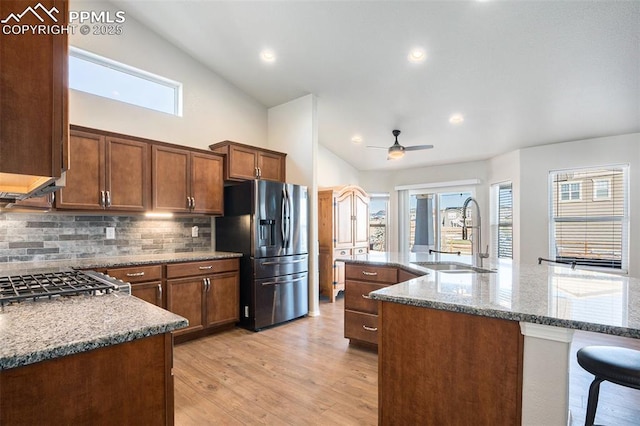 kitchen with stone counters, stainless steel refrigerator with ice dispenser, sink, and a kitchen island with sink