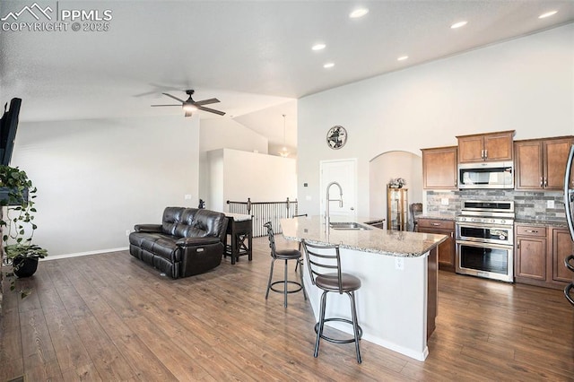 kitchen with sink, a center island with sink, stainless steel appliances, light stone counters, and a kitchen bar