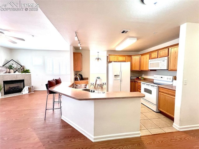 kitchen featuring sink, white appliances, ceiling fan, a kitchen breakfast bar, and a fireplace