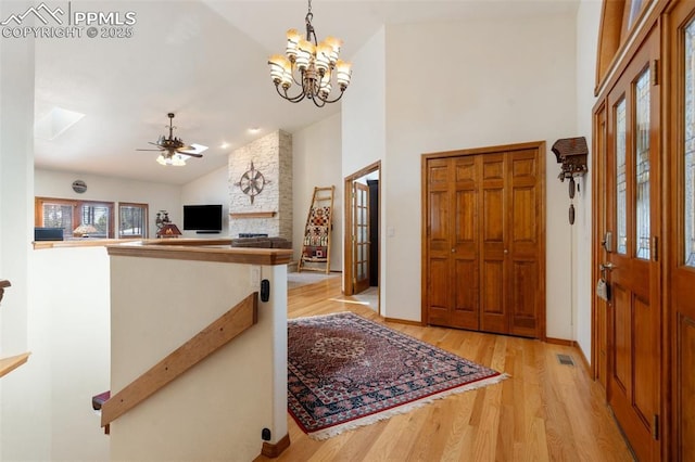 entryway featuring ceiling fan with notable chandelier, a large fireplace, high vaulted ceiling, and light hardwood / wood-style flooring