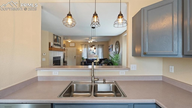 kitchen featuring sink, gray cabinets, ceiling fan, a fireplace, and decorative light fixtures