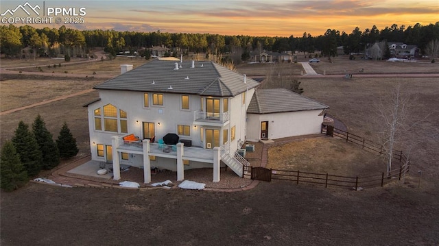 back house at dusk featuring a balcony and a patio