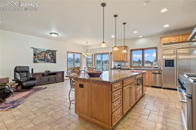 kitchen with sink, hanging light fixtures, a kitchen island, high end appliances, and stone countertops