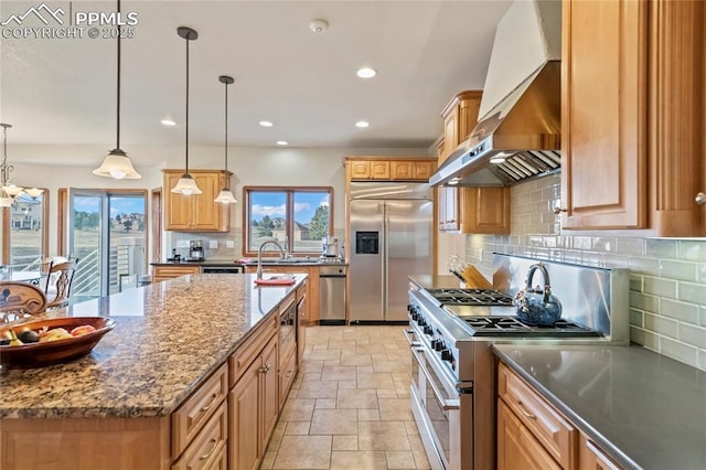 kitchen featuring extractor fan, decorative light fixtures, dark stone countertops, high quality appliances, and a kitchen island with sink