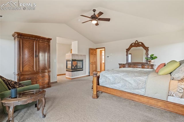 bedroom featuring a tiled fireplace, vaulted ceiling, light carpet, and ceiling fan