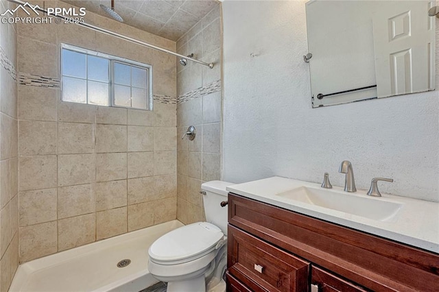 bathroom with a tile shower, vanity, and toilet