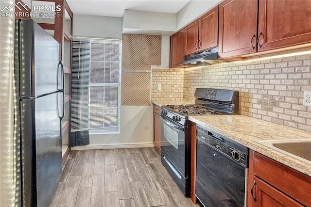 kitchen featuring backsplash, light stone countertops, light hardwood / wood-style flooring, and black appliances