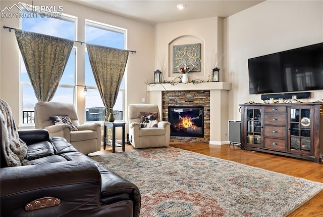 living room featuring wood-type flooring, plenty of natural light, and a stone fireplace