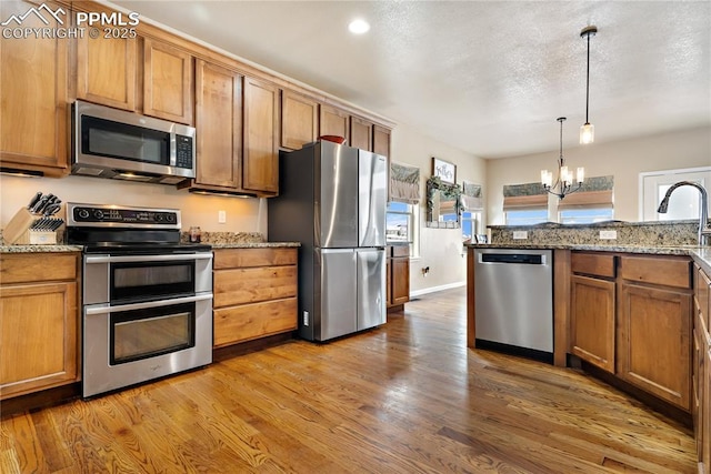 kitchen featuring hardwood / wood-style floors, pendant lighting, stainless steel appliances, light stone countertops, and an inviting chandelier