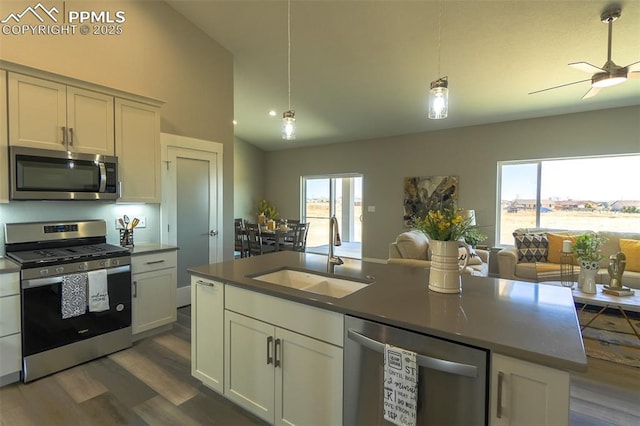 kitchen featuring appliances with stainless steel finishes, decorative light fixtures, an island with sink, sink, and dark wood-type flooring